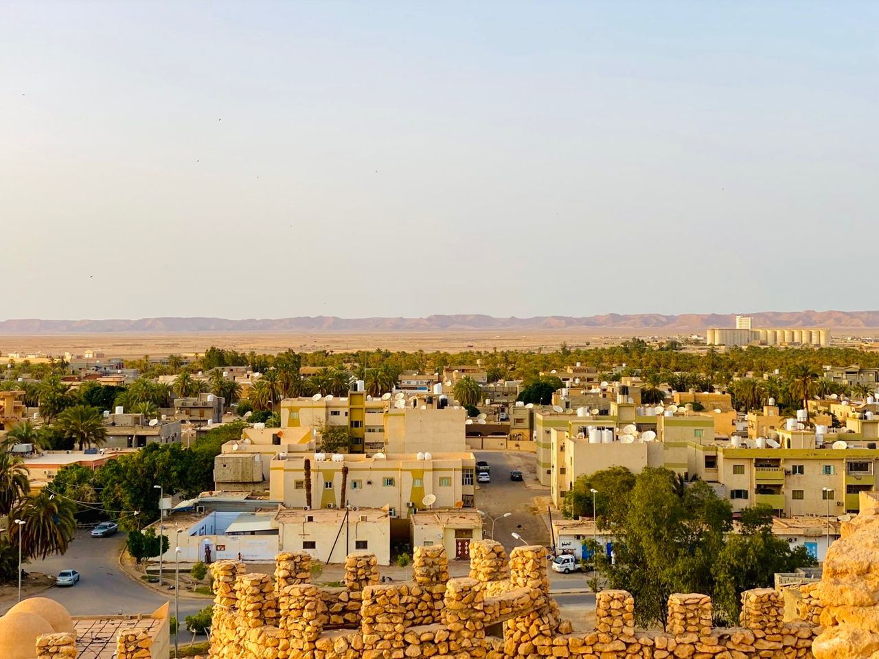 Panoramic view of Waddan city, its palm trees, surrounding desert, and distant grain silo.